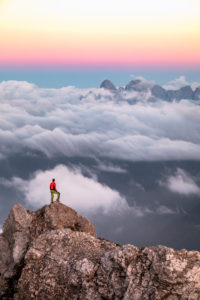 Lonely man stands on top of a mountain ridge, on the background a sea of clouds around the Agner mountain range, Pale di San Martino group, view from Costabella ridge, Dolomites, Italy Lonely man stands on top of a mountain ridge, on the background a sea of clouds around the Agner mountain range, Pale di San Martino group, view from Costabella ridge, Dolomites, Italy